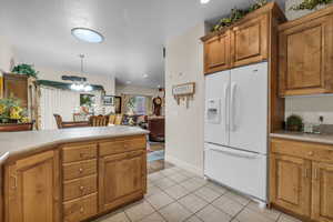 Kitchen with hanging light fixtures, white refrigerator with ice dispenser, and light tile patterned floors