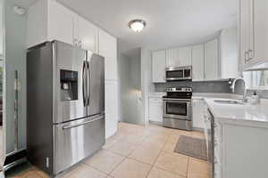 Kitchen featuring appliances with stainless steel finishes, light tile patterned flooring, sink, backsplash, and white cabinetry