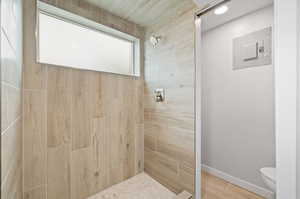 Bathroom with tiled shower, hardwood / wood-style floors, electric panel, and toilet