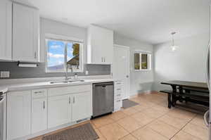 Kitchen with white cabinetry, hanging light fixtures, stainless steel appliances, and backsplash