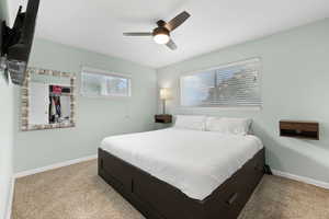 Carpeted bedroom featuring ceiling fan and multiple windows