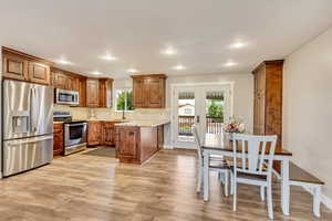 Kitchen featuring backsplash, sink, light stone countertops, appliances with stainless steel finishes, and light hardwood / wood-style floors