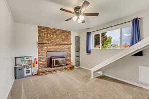 Unfurnished living room with ceiling fan, a wood stove, and carpet floors