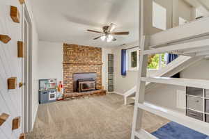 Carpeted living room with ceiling fan, wooden walls, and a fireplace