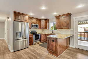 Kitchen featuring sink, light wood-type flooring, stainless steel appliances, light stone counters, and decorative backsplash