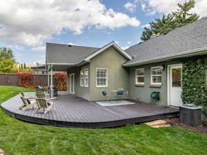 Rear view of house with a wooden deck, central AC, and a lawn