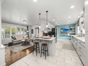 Kitchen featuring stainless steel refrigerator with ice dispenser, hanging light fixtures, kitchen peninsula, a breakfast bar, and white cabinetry with view of formal living room.