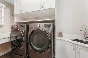 Clothes washing area featuring cabinets, sink, and separate washer and dryer