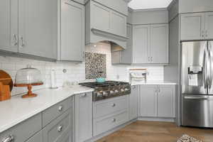 Kitchen with appliances with stainless steel finishes, light hardwood / wood-style flooring, decorative backsplash, and gray cabinets