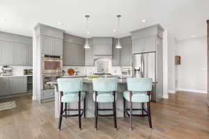 Kitchen featuring hanging light fixtures, backsplash, appliances with stainless steel finishes, premium range hood, and light hardwood / wood-style flooring