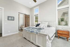 Bedroom with a barn door, light colored carpet, ensuite bath, and ceiling fan