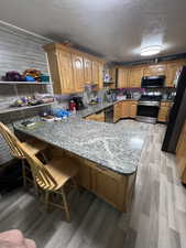 Kitchen with kitchen peninsula, a breakfast bar area, black appliances, light hardwood / wood-style floors, and sink