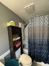 Bathroom with shower / bath combo, a textured ceiling, and toilet