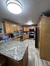 Kitchen featuring light wood-type flooring, black appliances, a textured ceiling, and kitchen peninsula