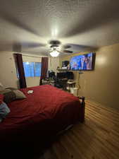 Bedroom featuring ceiling fan, hardwood / wood-style flooring, and a textured ceiling