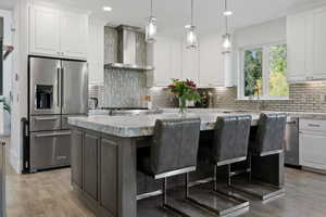 Kitchen featuring wall chimney exhaust hood, a center island, high quality fridge, white cabinetry, and light stone counters