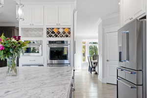 Kitchen featuring hanging light fixtures, appliances with stainless steel finishes, white cabinetry, light wood-type flooring, and ornamental molding