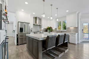 Kitchen featuring a kitchen island, wall chimney range hood, high quality fridge, white cabinets, and light stone counters