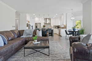 Living room featuring sink, crown molding, wood-type flooring, and an inviting chandelier