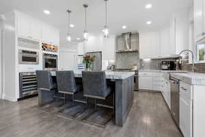 Kitchen with wall chimney range hood, a center island, white cabinetry, stainless steel appliances, and wine cooler