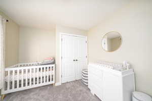 Bedroom with a closet, light colored carpet, and a crib