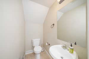 Bathroom featuring sink, toilet, tile patterned floors, and lofted ceiling