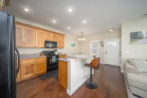 Kitchen with dark laminate flooring, black appliances, decorative light fixtures, and a kitchen island