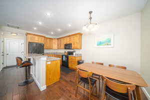 Kitchen featuring black appliances, dark laminate flooring, decorative light fixtures, and a kitchen island