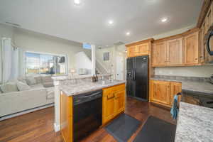 Kitchen with dark laminate floors, black appliances, sink, and an island with sink