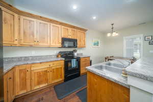 Kitchen with dark laminate floors, sink, black appliances, decorative light fixtures, and an inviting chandelier