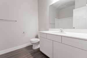Bathroom featuring walk in shower, baseboards, toilet, wood finished floors, and vanity
