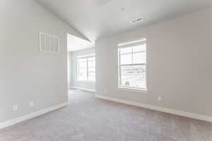 Carpeted spare room featuring baseboards, a textured ceiling, visible vents, and vaulted ceiling