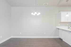 Unfurnished dining area featuring dark wood finished floors, a notable chandelier, and visible vents