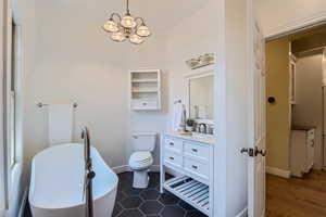 Bathroom featuring an inviting chandelier, toilet, a bath, vanity, and tile patterned floors