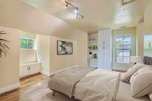 Bedroom with lofted ceiling, a textured ceiling, light hardwood / wood-style flooring, and multiple windows