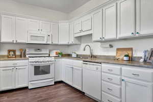 Kitchen featuring sink, white cabinetry, dark hardwood / wood-style floors, and white appliances