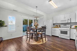 Kitchen featuring white cabinets, decorative light fixtures, dark wood-type flooring, and white appliances