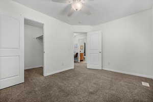 Unfurnished bedroom featuring a spacious closet, carpet flooring, a closet, and ceiling fan