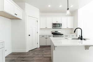 Kitchen featuring appliances with stainless steel finishes, sink, a breakfast bar, pendant lighting, and white cabinets