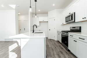 Kitchen with a center island with sink, appliances with stainless steel finishes, sink, white cabinetry, and hanging light fixtures