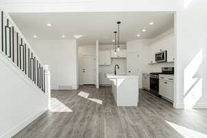 Kitchen with appliances with stainless steel finishes, light hardwood / wood-style flooring, decorative light fixtures, white cabinets, and an island with sink