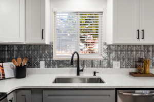 Kitchen featuring sink, white cabinetry, stainless steel dishwasher, light stone counters, and decorative backsplash