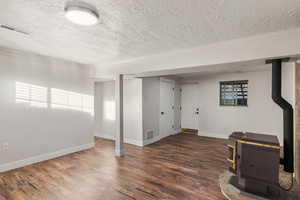 Basement with crown molding, a textured ceiling, a wood stove, and dark hardwood / wood-style flooring