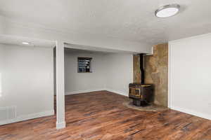 Basement featuring hardwood / wood-style floors, a textured ceiling, and a wood stove