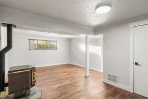 Basement featuring wood-type flooring, a textured ceiling, a wood stove, heating unit, and ornamental molding