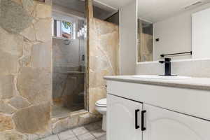 Bathroom with vanity, walk in shower, toilet, and tile patterned flooring