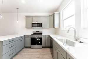 Kitchen featuring kitchen peninsula, gray cabinetry, decorative light fixtures, sink, and appliances with stainless steel finishes