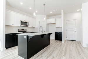 Kitchen featuring sink, pendant lighting, stainless steel appliances, white cabinets, and an island with sink