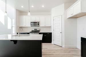 Kitchen with hanging light fixtures, white cabinetry, appliances with stainless steel finishes, and sink