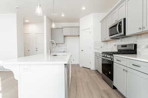 Kitchen with a center island with sink, appliances with stainless steel finishes, sink, pendant lighting, and light hardwood / wood-style floors